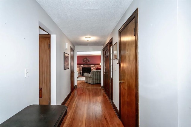 hall with a textured ceiling, baseboards, and wood finished floors