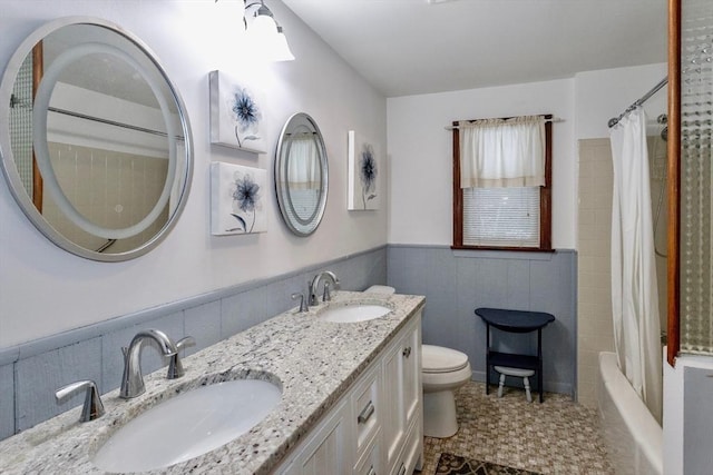 full bath with a wainscoted wall, a sink, toilet, and double vanity