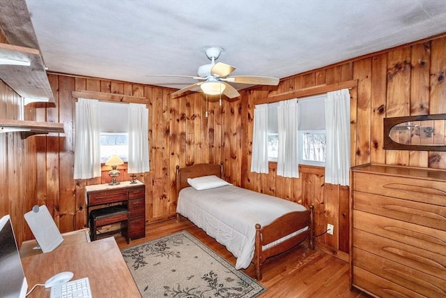 bedroom featuring wood walls, a ceiling fan, and wood finished floors