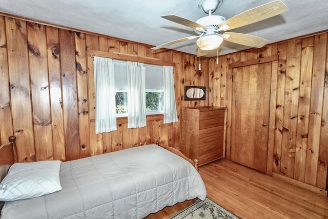 bedroom with wood walls, a ceiling fan, and wood finished floors