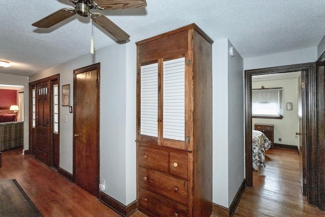 hall featuring a textured ceiling, wood finished floors, and baseboards