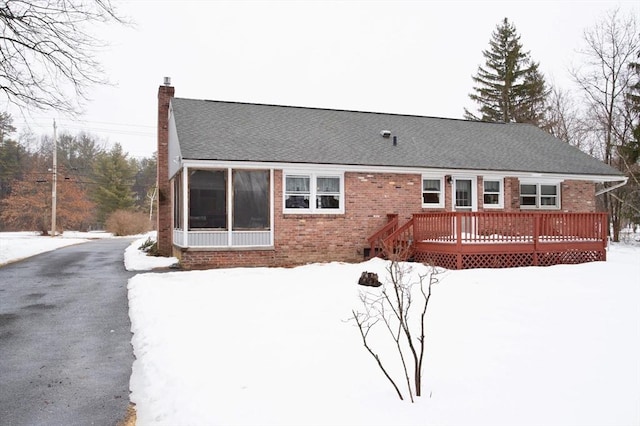 snow covered rear of property with roof with shingles, brick siding, a chimney, and a wooden deck