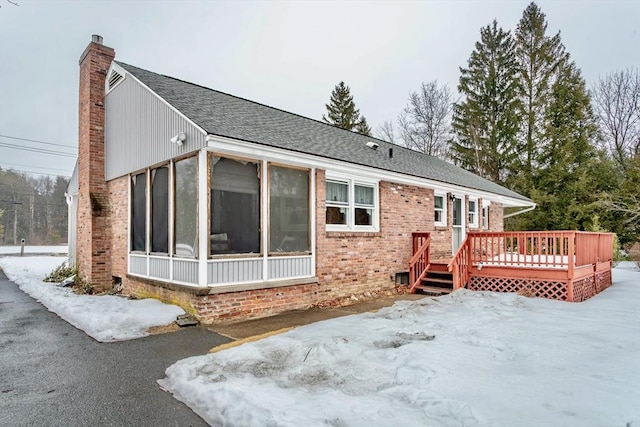 exterior space with a deck, brick siding, a sunroom, roof with shingles, and a chimney