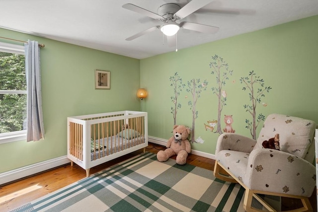 85 Green Meadow Ct, Northbridge, MA 01588 - bedroom featuring a crib, wood finished floors, baseboards, a ceiling fan, and a baseboard heating unit