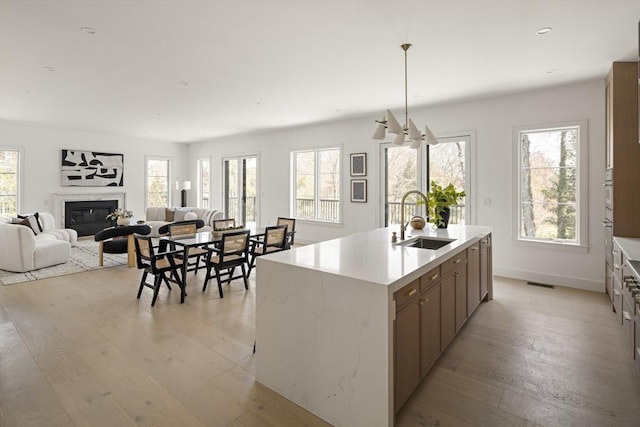 kitchen with a sink, light wood-style flooring, a glass covered fireplace, baseboards, and recessed lighting