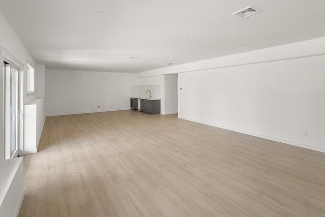 unfurnished living room featuring a sink, light wood finished floors, and baseboards