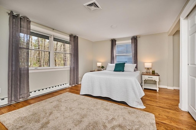 bedroom with baseboards, a baseboard radiator, wood finished floors, and visible vents