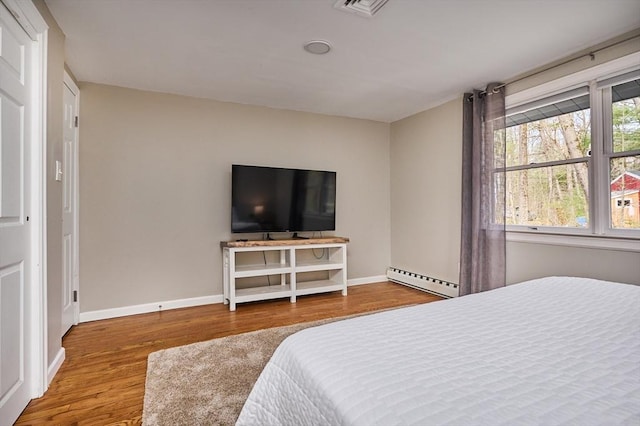 bedroom featuring wood finished floors, baseboards, a baseboard heating unit, and visible vents