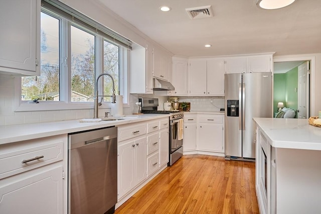 kitchen featuring visible vents, appliances with stainless steel finishes, tasteful backsplash, a sink, and under cabinet range hood