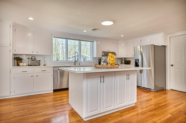 kitchen with appliances with stainless steel finishes, light countertops, white cabinetry, a kitchen island, and visible vents