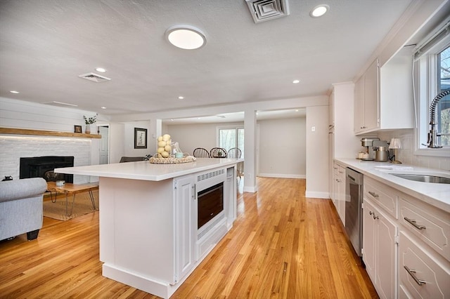 kitchen featuring visible vents, a fireplace, white cabinetry, a sink, and light wood finished floors