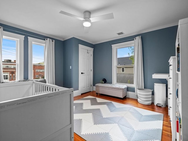 bedroom with ceiling fan, visible vents, light wood-type flooring, baseboards, and ornamental molding
