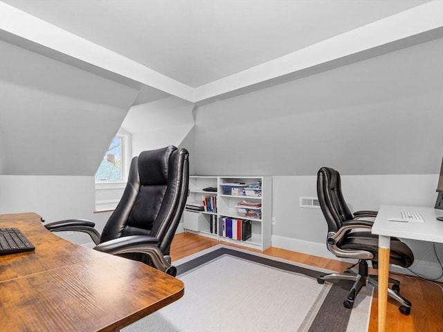 office area with baseboards, wood finished floors, vaulted ceiling, and visible vents