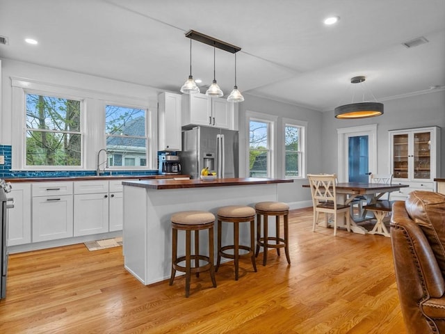 kitchen featuring a kitchen island, visible vents, a sink, stainless steel fridge with ice dispenser, and white cabinets