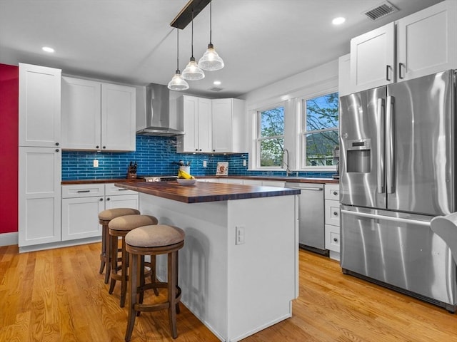 kitchen with visible vents, a kitchen island, wooden counters, wall chimney range hood, and stainless steel appliances