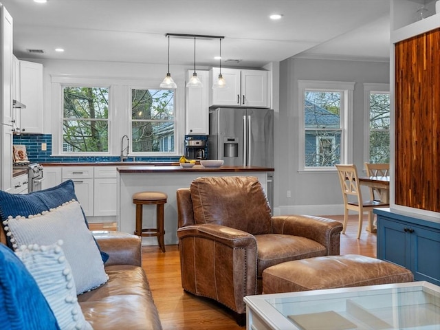 living area featuring light wood finished floors, recessed lighting, baseboards, visible vents, and ornamental molding