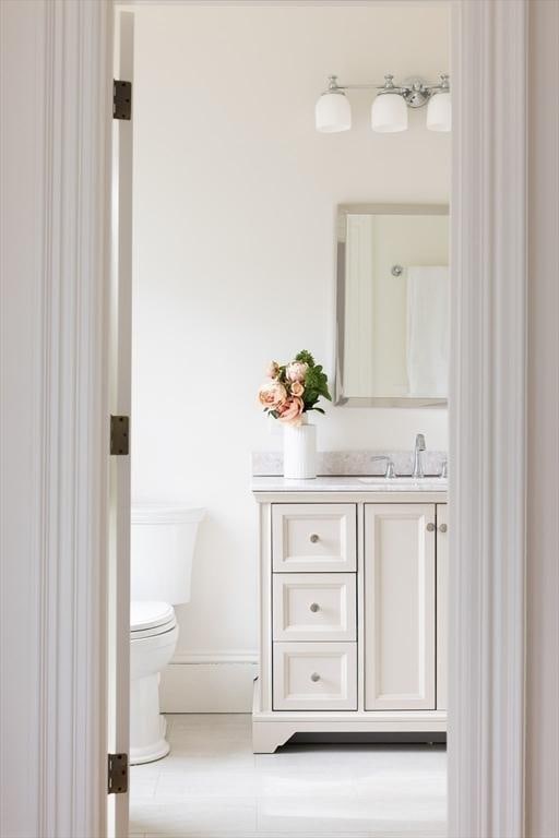 half bath featuring baseboards, toilet, and vanity