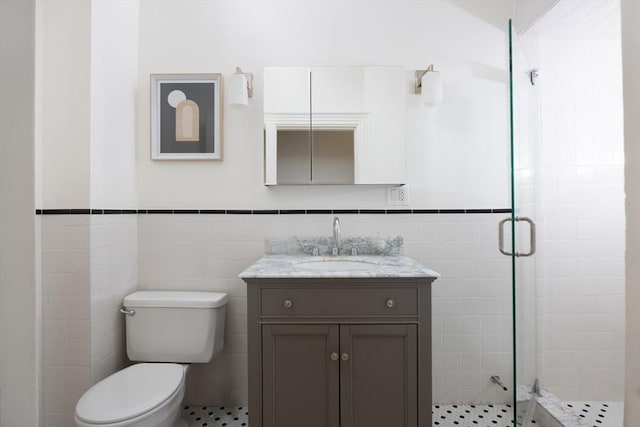 full bath featuring vanity, tile walls, a stall shower, and wainscoting