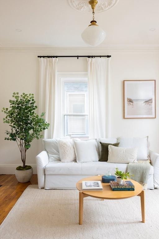 living area featuring wood finished floors, baseboards, and ornamental molding