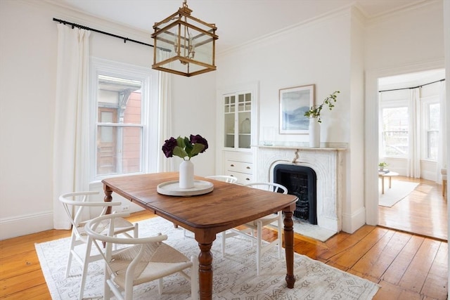 dining space featuring a high end fireplace, baseboards, light wood finished floors, and ornamental molding