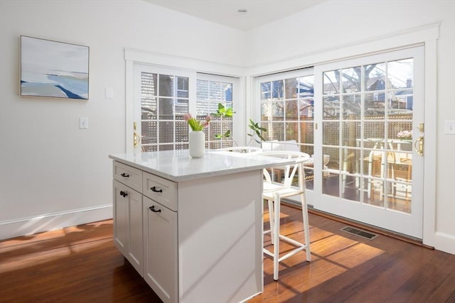 kitchen with visible vents, dark wood-type flooring, light stone counters, a breakfast bar area, and baseboards