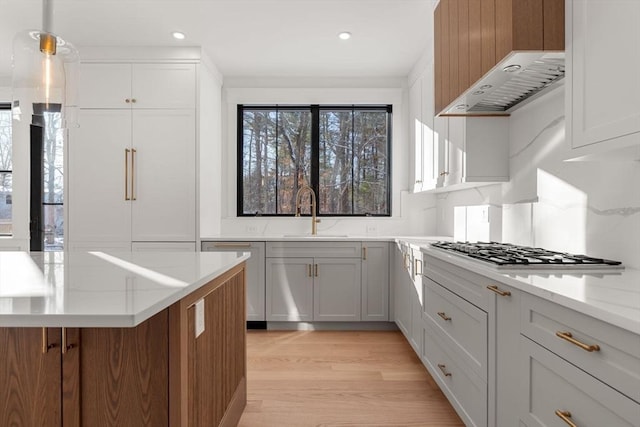 kitchen featuring light stone countertops, stainless steel gas cooktop, custom range hood, sink, and pendant lighting