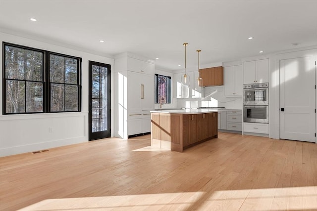 kitchen featuring a center island, light hardwood / wood-style floors, white cabinets, pendant lighting, and double oven