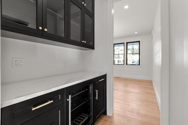 bar with light stone countertops, beverage cooler, and light wood-type flooring