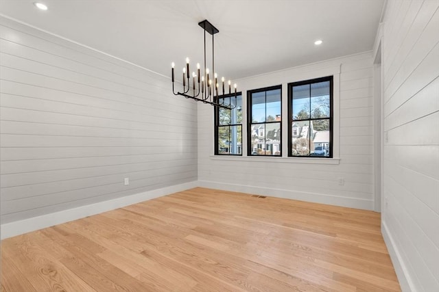 unfurnished dining area with wood walls, light wood-type flooring, an inviting chandelier, and ornamental molding