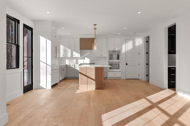 kitchen featuring decorative light fixtures, backsplash, white cabinetry, a kitchen island, and stainless steel double oven