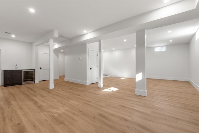 basement featuring light wood-type flooring, beverage cooler, and bar