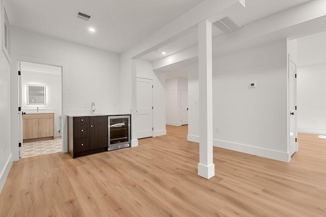 bar with sink, dark brown cabinetry, light hardwood / wood-style flooring, and beverage cooler