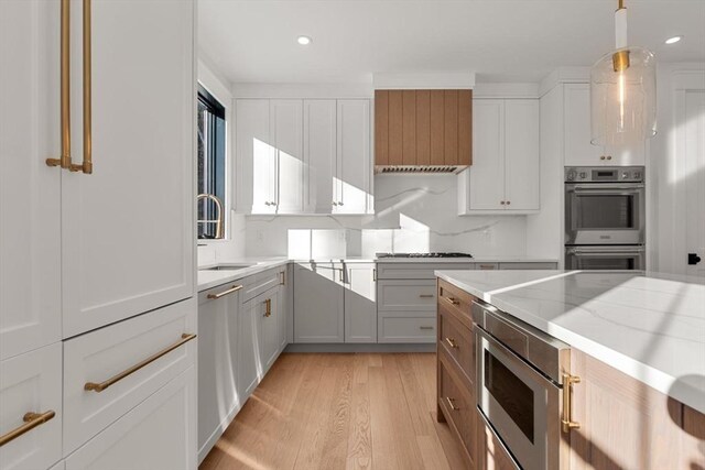 kitchen featuring light hardwood / wood-style floors, white cabinets, decorative light fixtures, sink, and stainless steel appliances