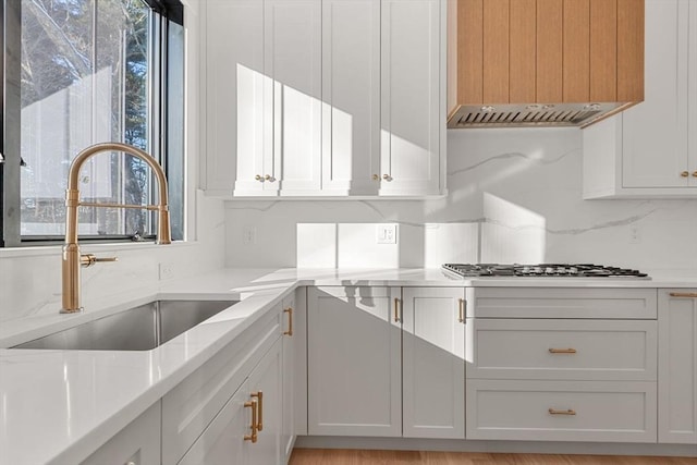 kitchen featuring sink, backsplash, white cabinets, and premium range hood