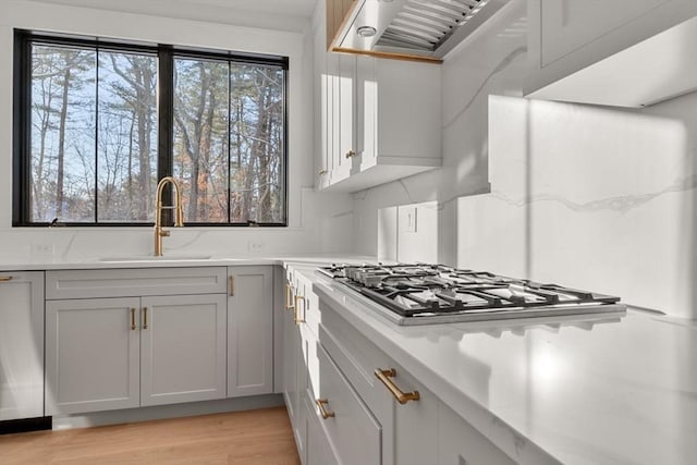 kitchen with sink, stainless steel gas stovetop, wall chimney exhaust hood, and gray cabinetry