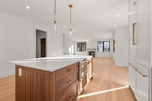 kitchen featuring decorative light fixtures, light wood-type flooring, white cabinetry, and a large island