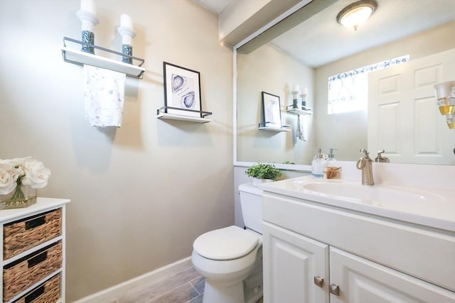 bathroom featuring toilet, baseboards, wood finished floors, and vanity