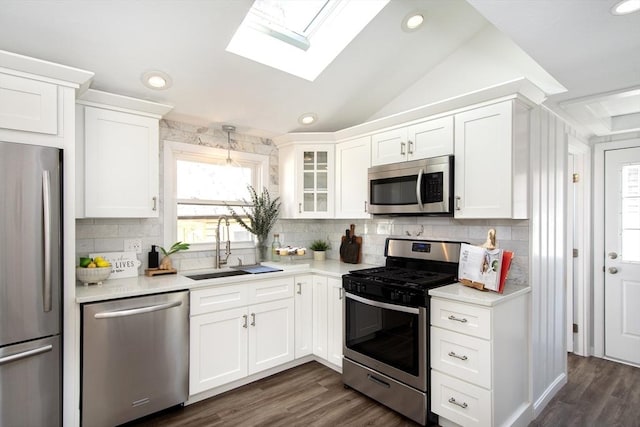 kitchen featuring stainless steel appliances, white cabinetry, sink, and vaulted ceiling with skylight