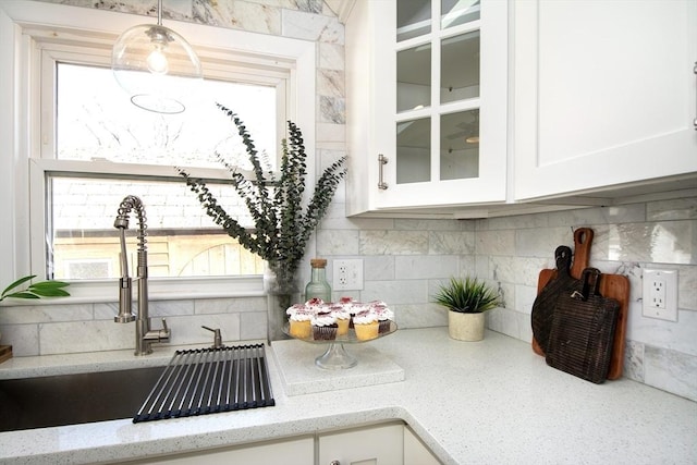 room details featuring white cabinetry, sink, backsplash, hanging light fixtures, and light stone countertops