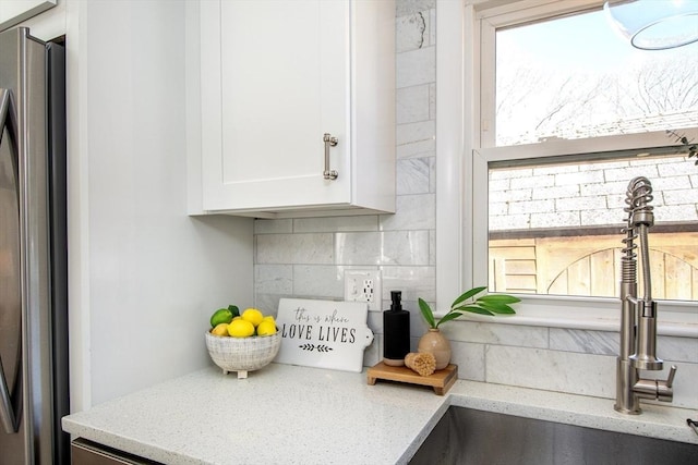 kitchen with sink, light stone counters, refrigerator, decorative backsplash, and white cabinets