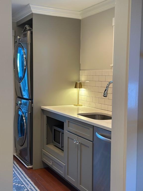 kitchen with ornamental molding, gray cabinets, stainless steel dishwasher, stacked washing maching and dryer, and a sink