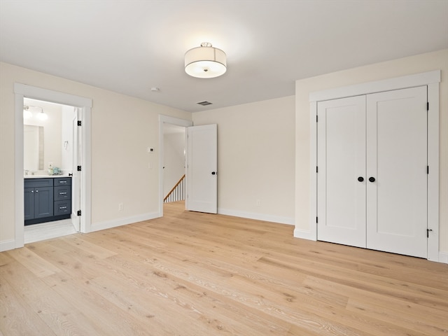 unfurnished bedroom with ensuite bathroom, light hardwood / wood-style floors, and a closet