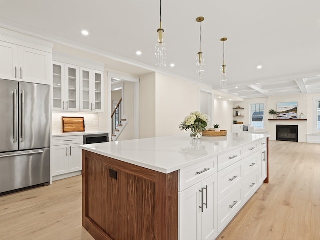 kitchen with stainless steel fridge, pendant lighting, white cabinetry, light hardwood / wood-style flooring, and a kitchen island