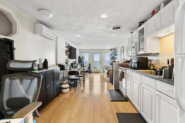 374 Humphrey St Unit 4, Swampscott, MA 01907 - kitchen featuring an AC wall unit, white cabinets, light wood-type flooring, white appliances, and glass insert cabinets