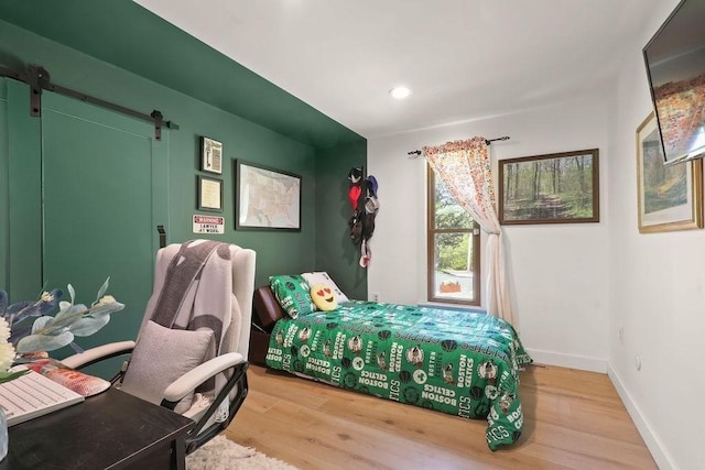 bedroom with light wood-style floors, a barn door, recessed lighting, and baseboards