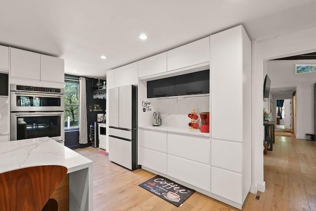 kitchen featuring freestanding refrigerator, double oven, light wood-style flooring, white cabinetry, and tasteful backsplash