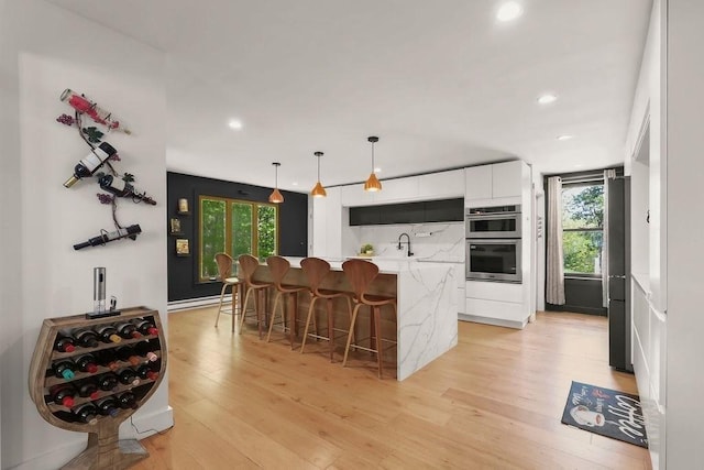 kitchen featuring white cabinets, an island with sink, double oven, light wood-style floors, and a sink