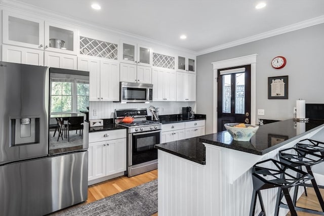 kitchen with ornamental molding, a breakfast bar area, appliances with stainless steel finishes, and white cabinets
