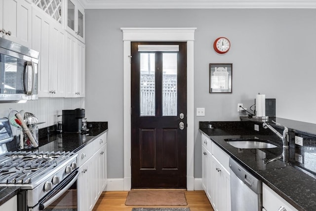 kitchen with appliances with stainless steel finishes, a sink, crown molding, white cabinets, and light wood-type flooring