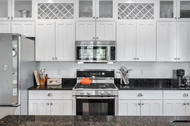 kitchen featuring white cabinetry, dark stone counters, appliances with stainless steel finishes, and glass insert cabinets